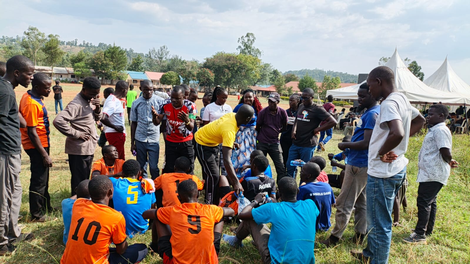 Young people in sports jerseys gathered in a circle on a field at the NET fun day